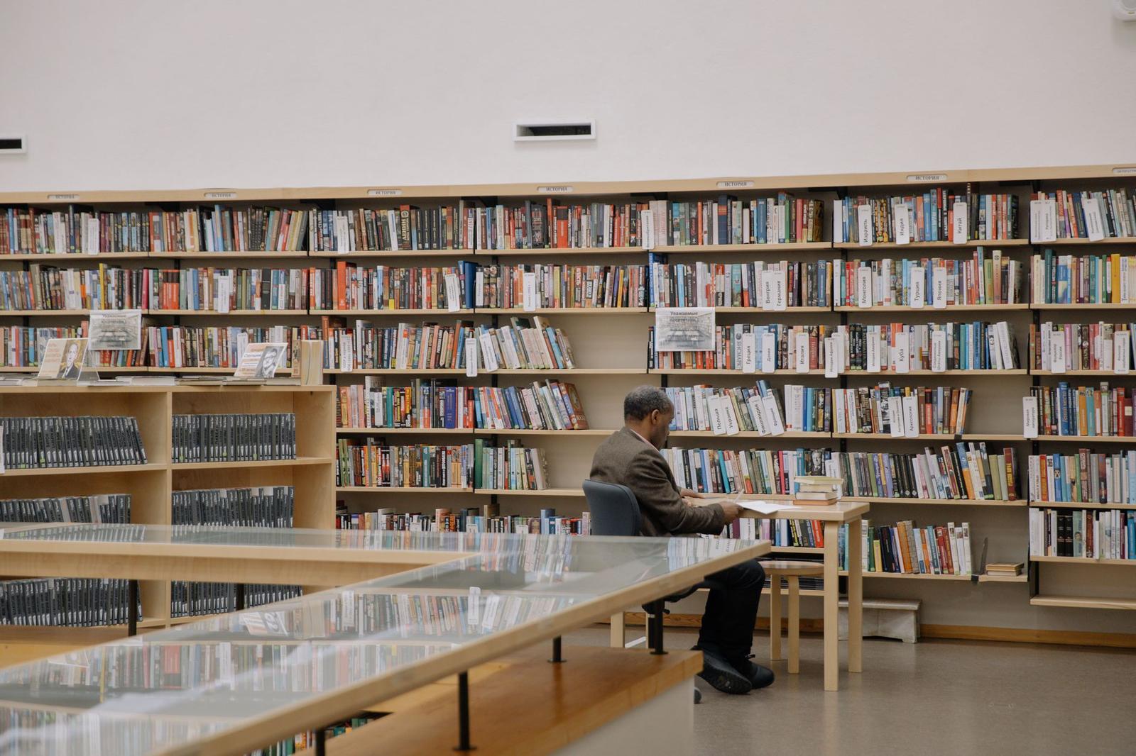 Man in Black Suit Jacket Reading Inside a Library